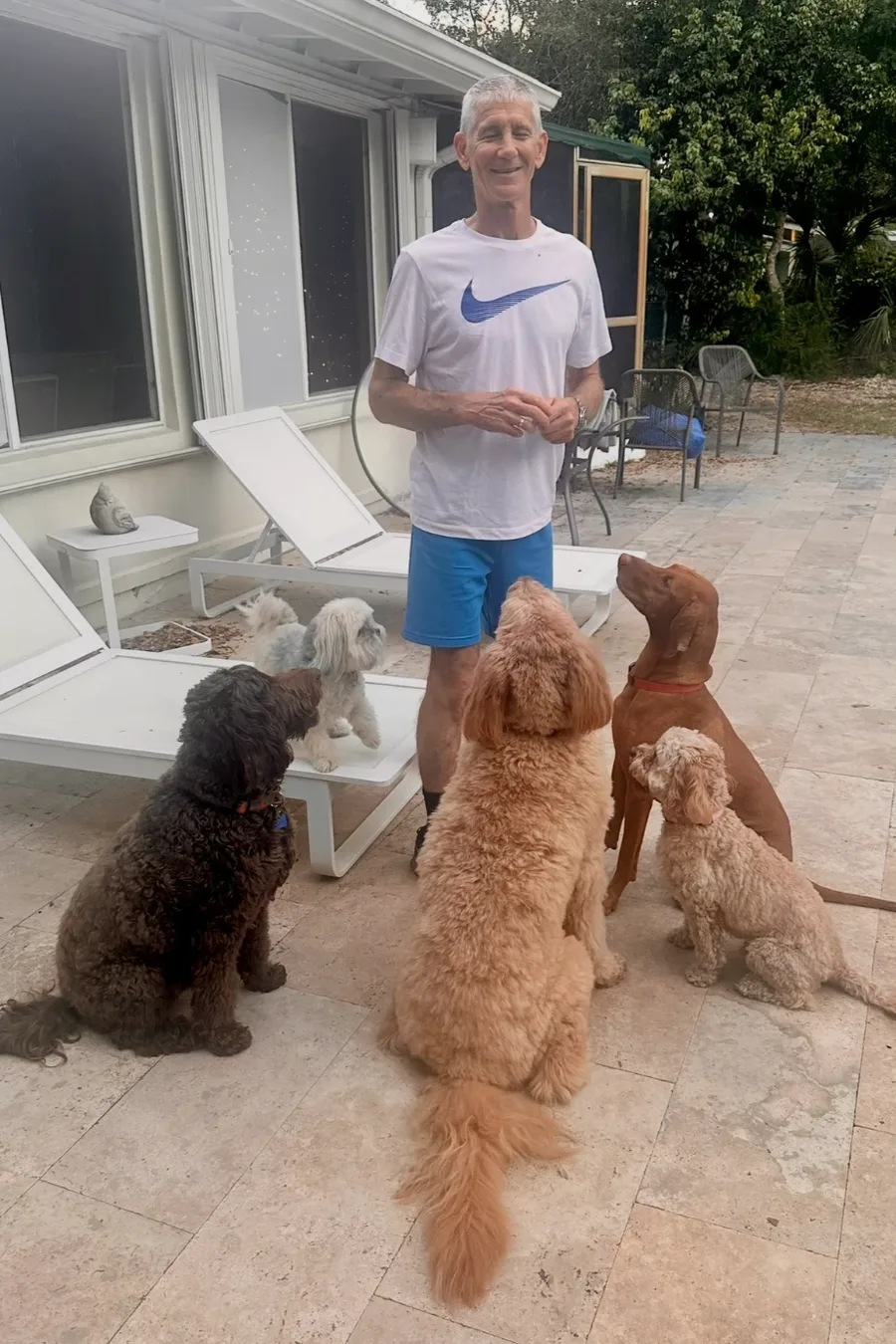 Andrew on the back patio with five boarding dogs sitting and looking up at him